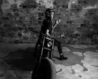 Modelo con casco y camiseta negra, posando sobre motocicleta clásica en espacio industrial