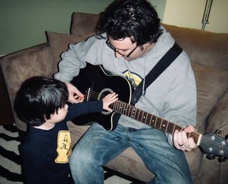 A father sitting while playing guitar with his toddler