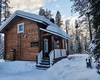 Snow covered log cabin set in lapland surrounded by forrests on a clear day