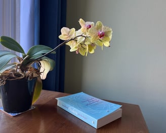 Part of a desk in a psychotherapy practice room with on it a book and a flower