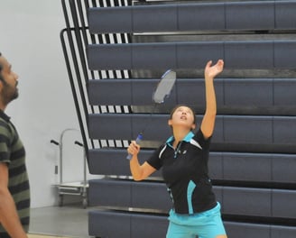 Ellen  preparing to serve during a badminton match in an indoor gym.