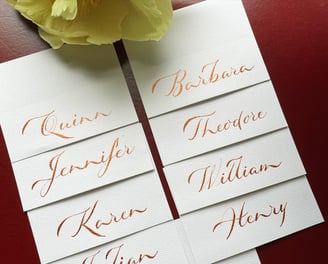 Beautiful calligraphy place cards in metallic bronze ink on white paper showcased on red background 