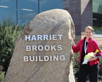 Ellen poses with flowers next to large stone sign that says "Harriet Brooks Building"