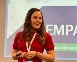 a woman in a red shirt and black pants speaking in front of a screen saying Empathy
