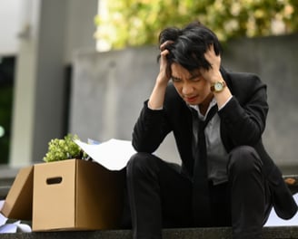 Pria muda duduk di tangga dengan ekspresi stres dan kotak barang pribadi di sampingnya setelah kehilangan pekerjaan