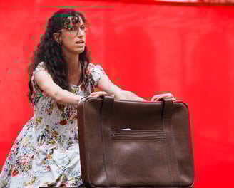 comédienne chanteuse sur scène équipée d'un micro serre tête, en train d'ouvrir une valise
