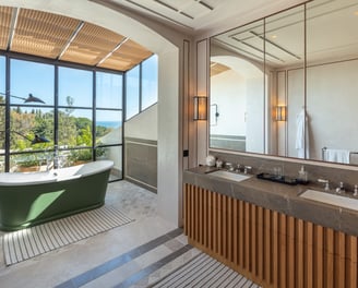 Bathroom with freestanding green tub, double vanity, and floor-to-ceiling garden view windows.