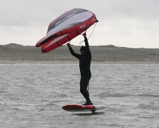 Un homme tient sa wing sur sa planche de wingfoil