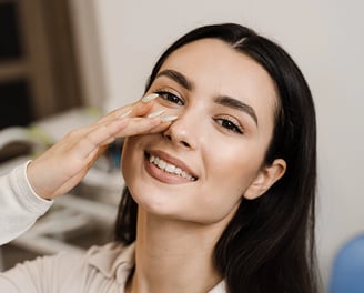 Smiling woman gently touches her nose, showing satisfaction.