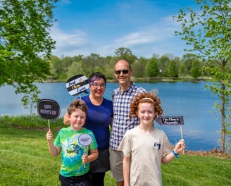 Two parents and two children posing in front of a lake holding sign props