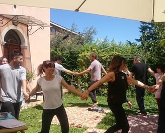 a group of people holding hands and dancing in a garden, classe di bioenergetica
