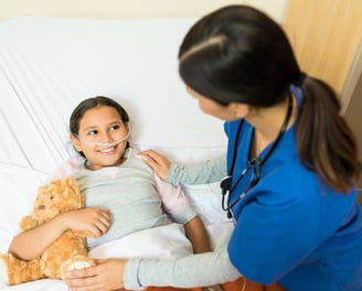 A young girl lies in a hospital bed , receiving care from a female doctor.