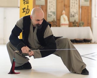 Ismet Himmet demonstrating a low Wudang sword stance (Jian) during indoor training with altar behind.