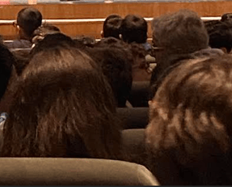 a man in a suit and tie is standing in front of a lecture hall