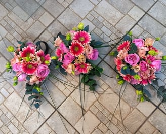 Trei buchete pastel cu trandafiri roz, gerbera și lisianthus, așezate pe podea cu model geometric.