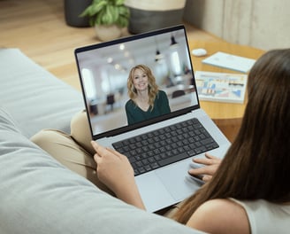 a woman sitting on a couch with a laptop computer screen showing a video chat