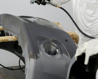 a man in a white suit and a white coat painting a car at fix collision center