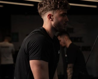 Barbat la sala, executa extensii pentru triceps la scripete, imbracat in negru.