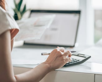 Woman managing monthly bookkeeping, using a calculator and computer to organize financial records.