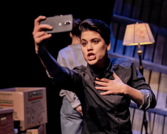 A young person with short hair holds their phone out to record a video of themselves talking