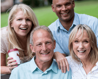 a group of four adults of diverse races sitting on a bench in a park