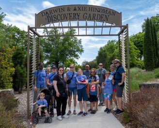 Group photo of adults and children posed on a paved walkway under an entry to a garden