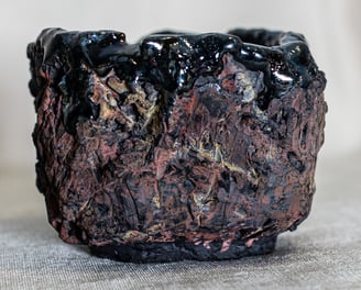 Raku-fired Kurinuki cup from Amman, Jordan, with black glaze, ochre tones, and volcanic textures