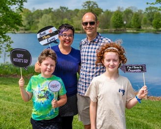 A family of four posing in front of a lake holding paper props