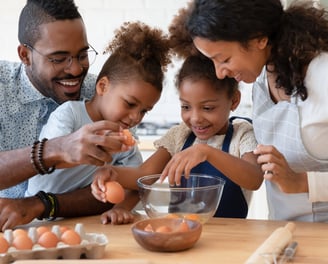 a family breaking eggs as they prepare food together