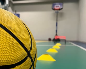 Primo piano di un pallone da basket giallo in un'area multisport della palestra Move 2 Grow a Milano, con coni e canestro sul