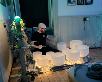 a man playing crystal bowls at night with fairy lights all around