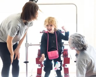 Dos personas adultas ayudando a un niño con paralisis cerebral con fisioterapia