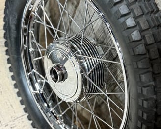 a motorcycle vintage hand polished wheel with a knobbie tire in front of wooden wall.