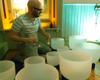 a man is sitting on a floor playing crystal bowls