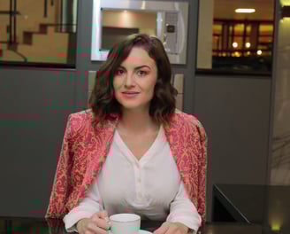 35+ woman mentor at a counter, dressed in pink and white, holding a cup of coffee