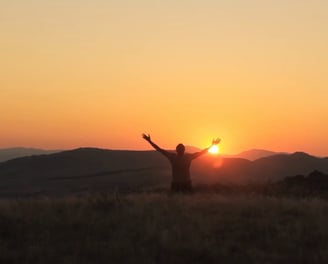 a person standing on a hill with their arms up in the air