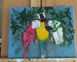 Progress photo of three macaws painting on a wooden easel.