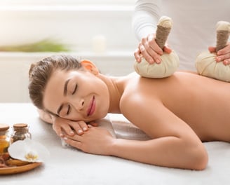 Ontspannende rugmassage met kruidenstempels in een wellness setting.