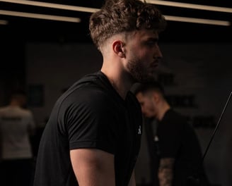 Barbat la sala, executa extensii pentru triceps la scripete, imbracat in negru.