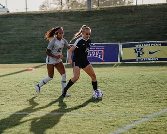 Two soccer players competing on a field, one in white and black, the other in dark blue and white