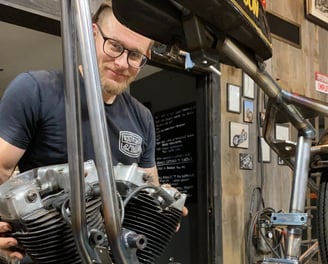 a man holding an engine behind a motorcycle frame.