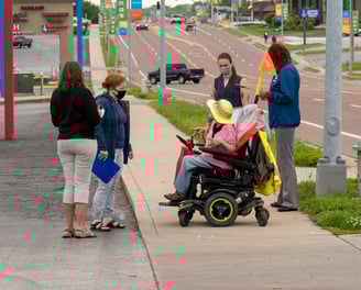 Group gathered on the sidewalk of a busy street