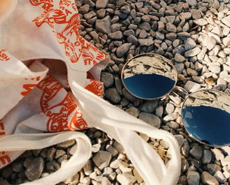 Foto de óculos de sol e bolsa de tecido sob pedras pequenas.