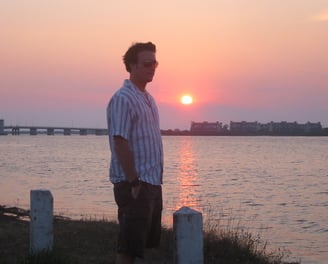 A man standing in front of the ocean with a sunset