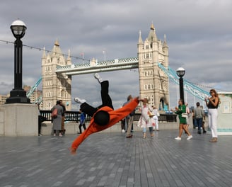 YoYo breakdancing with Tower Bridge, London, in the background as passers-by watch.