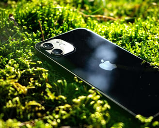 iPhone Km0 negro sobre musgo verde, destacando la sostenibilidad y la integración de la tecnología con la naturaleza.