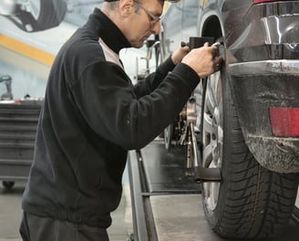 a man in a black jacket is aligning a frame of a car at fix collision center