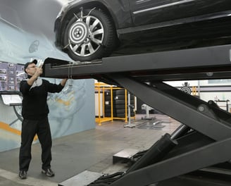 a man standing on a lift with a car on the lift trying to align its frame at fix collision center