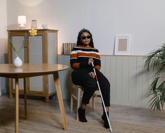 Blind woman with walking stick sitting in a chair beside a dining room table
