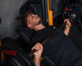 Barbat face impins la piept cu bara pe banca inclinata, echipat in negru.